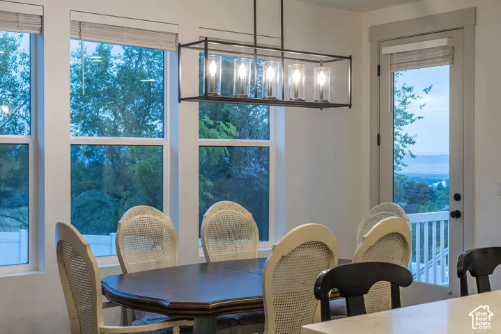 Dining area with a linear chandelier, multiple windows, and a glass-paned door opening to an exterior railing