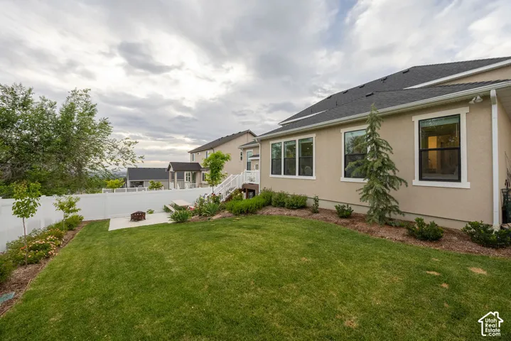 Expansive backyard featuring a manicured lawn, concrete patio with a built-in fire pit, and white vinyl fencing