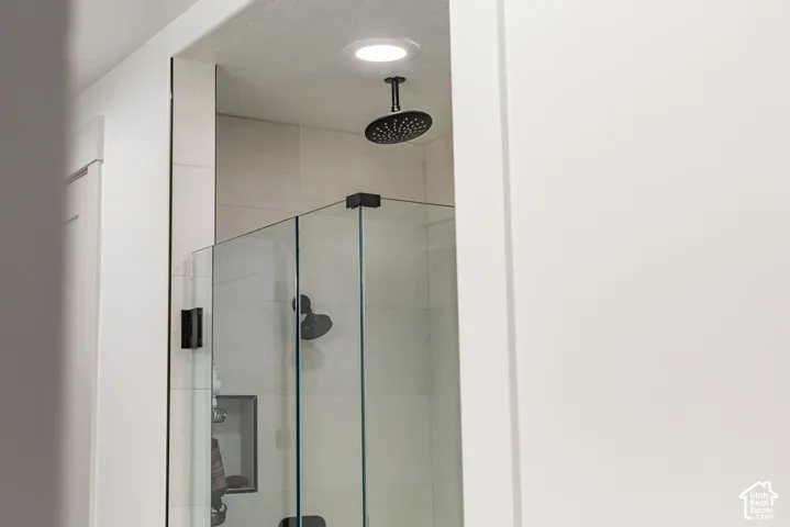 Frameless glass shower enclosure featuring a ceiling-mounted matte black rain shower head, large format tile surround, and a recessed shower niche