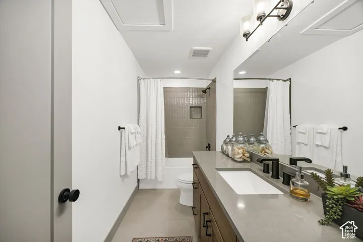 Bathroom featuring a large vanity with an integrated sink and matte black fixtures, a full-width mirror, tile flooring, and a bathtub with tiled surround and shower niche