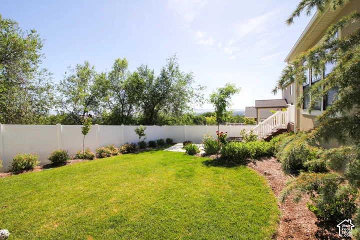 Expansive backyard featuring a manicured lawn, a white privacy fence, mature trees, a multi-level deck with white railings, and integrated landscaping