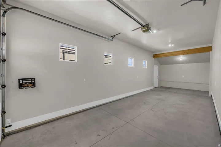 Spacious garage with concrete flooring, multiple windows, exposed wood beam, recessed lighting, and a white access door