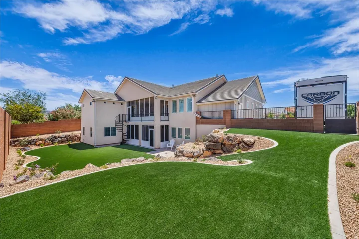 Expansive backyard featuring artificial turf, a rock-lined flower bed, and a screened-in patio
