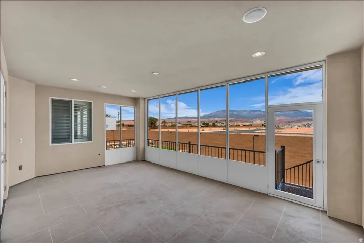 Enclosed patio featuring floor-to-ceiling windows, tile flooring, recessed lighting, and a glass-paneled door leading to an outdoor balcony