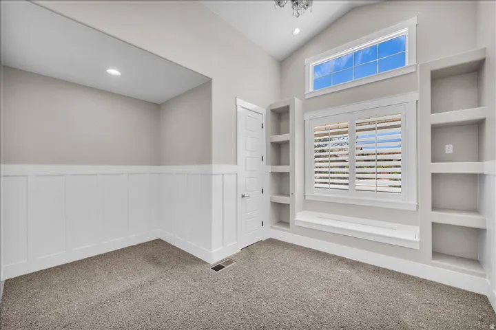 Vaulted ceiling room featuring built-in shelving, two windows with plantation shutters, a window bench, and recessed lighting