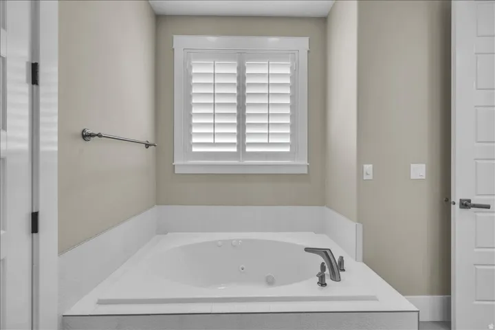 Built-in soaking tub with deck-mounted faucet and shower head, surrounded by a tiled deck and wainscoting