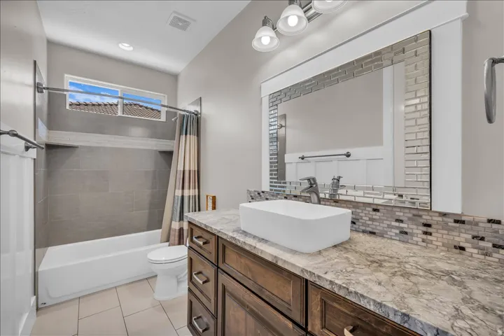 Full bathroom featuring a single vanity with a vessel sink, a multi-tone tile backsplash, and a framed mirror