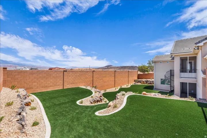 Expansive backyard featuring artificial turf, decorative rock landscaping, and a privacy wall