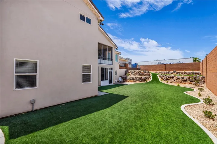 Expansive backyard featuring artificial turf, a decorative rock garden, and a concrete paver border
