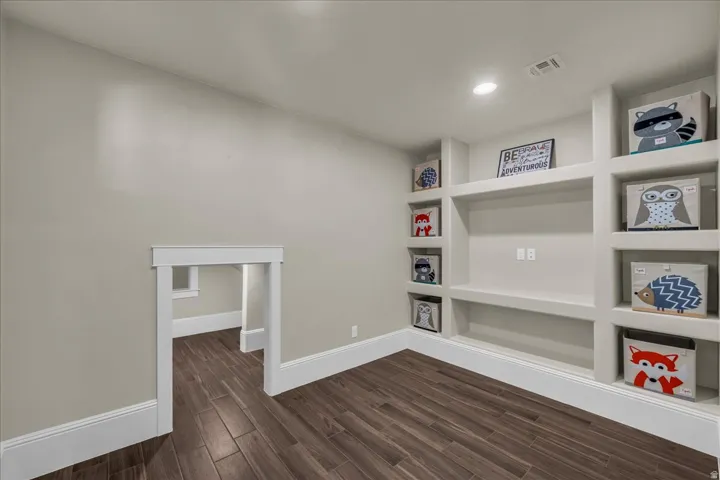Built-in shelving unit with integrated lighting, wood-finish flooring, white baseboards, and a framed doorway opening