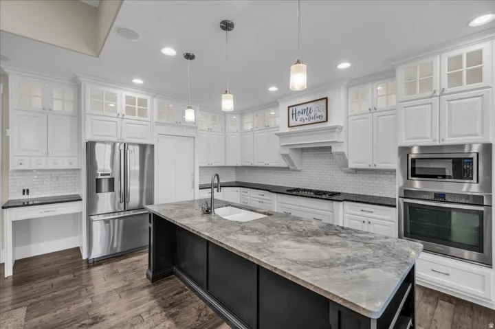 Contemporary kitchen featuring white cabinetry, wood-finish flooring, a large island with a double basin sink, stainless steel appliances, and pendant lighting