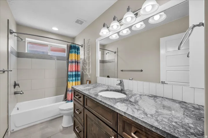 Bathroom featuring a dark wood-finish vanity with a stone countertop, an undermount sink, and a large mirror with track lighting