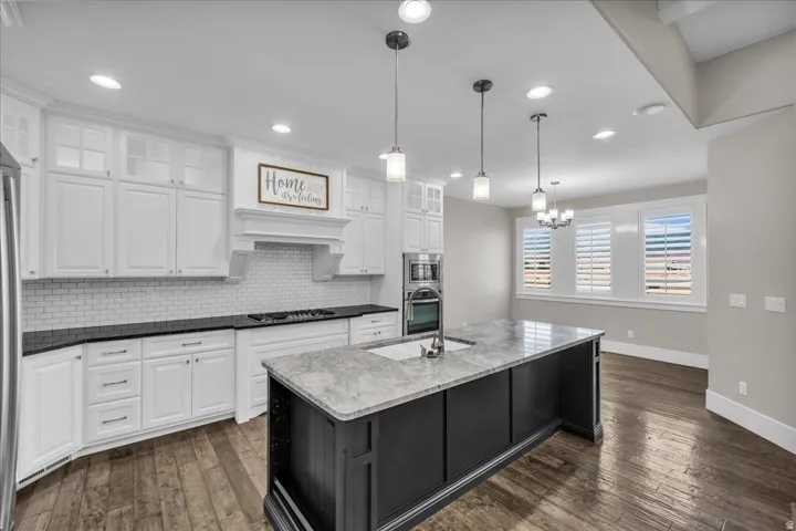 Kitchen featuring white shaker-style cabinetry, a built-in double oven, a central island with an integrated sink, a white subway tile backsplash, and wood-finish flooring