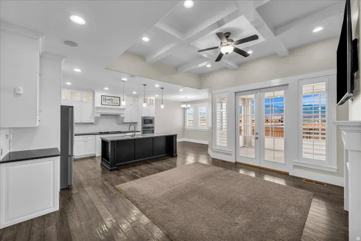 Open-concept living space featuring wood-finish flooring, a coffered ceiling with recessed lighting, and a ceiling fan