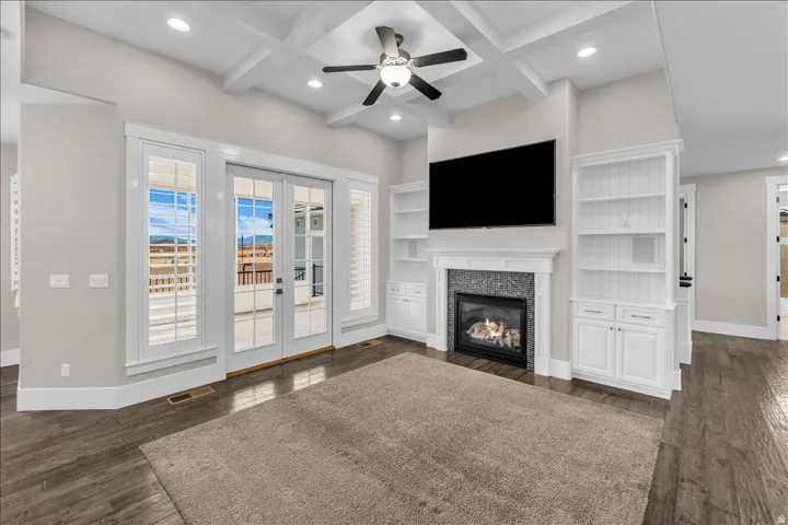 Living area featuring a coffered ceiling, wood-finish flooring, a fireplace with a stone surround, and built-in cabinetry