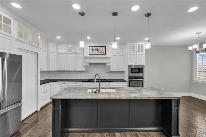 Kitchen featuring an expansive island with a stone countertop, white shaker cabinetry with glass-front uppers, a subway tile backsplash, and stainless steel appliances