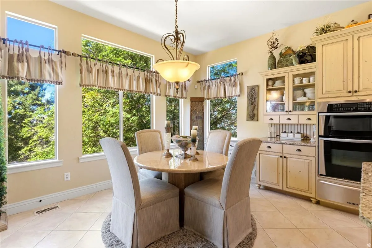 Expansive window array surrounding a dining area with a circular pedestal table, complemented by built-in cabinetry featuring glass display doors and a double wall oven