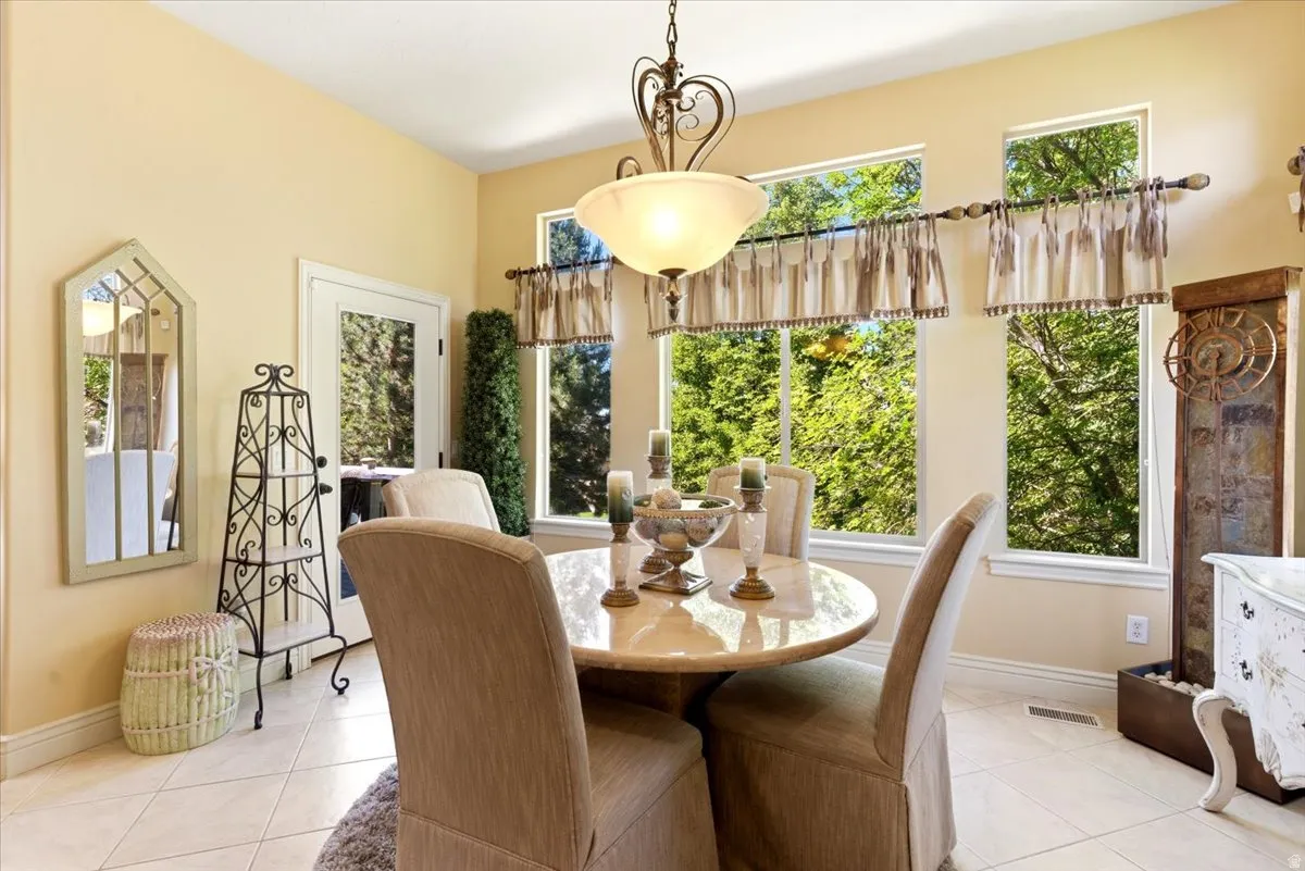 Dining area featuring a central chandelier, multiple large windows, tile flooring, a glass-paned exterior door, and detailed baseboards