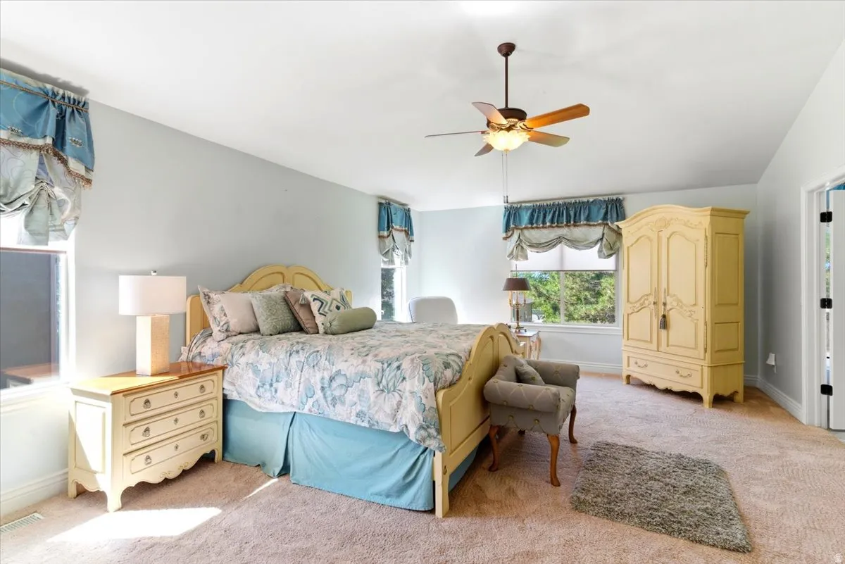 Bedroom featuring light wall color, carpet flooring, a ceiling fan, and multiple windows