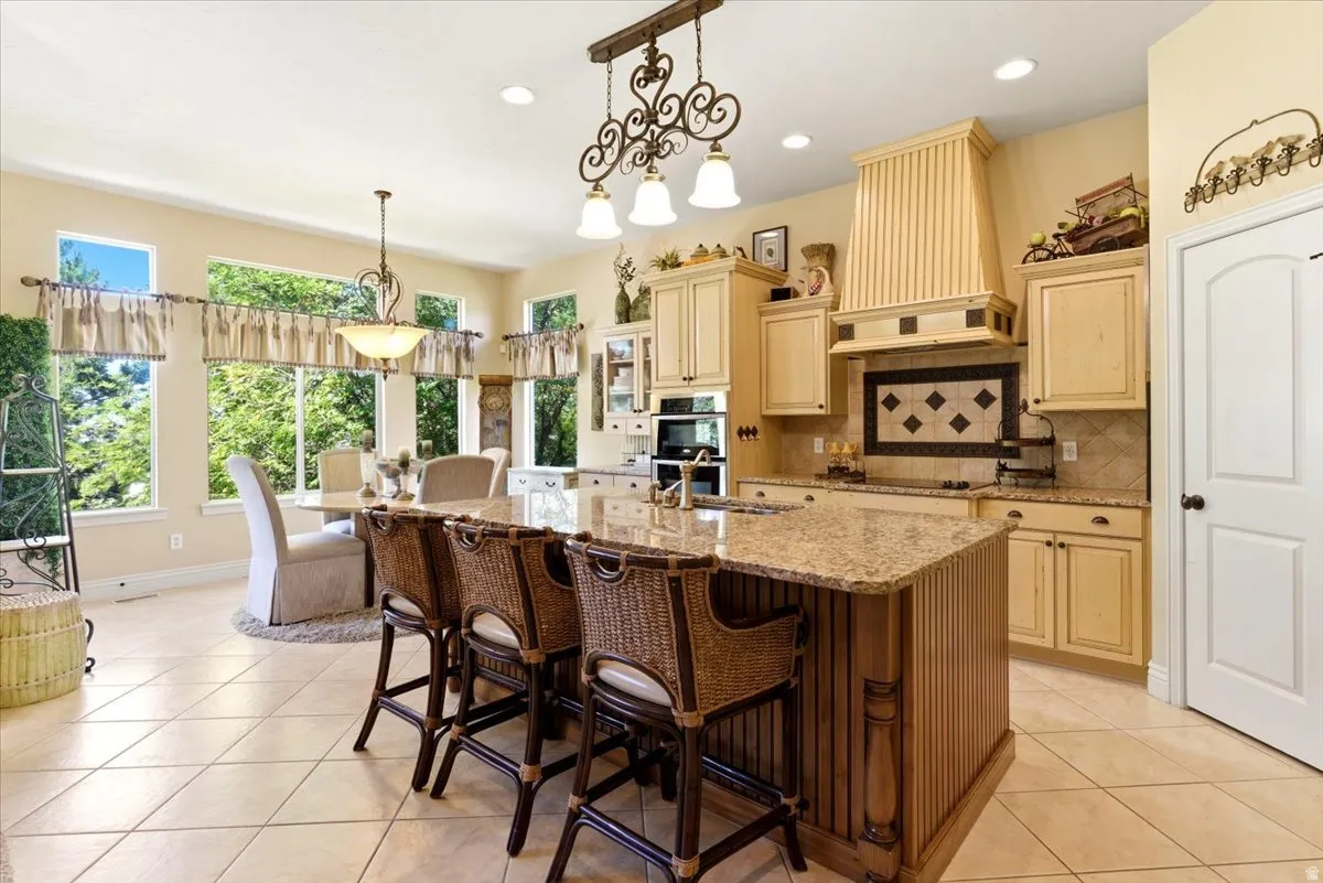 Kitchen featuring a large central island with bar seating, light-toned cabinetry, a custom range hood, and a decorative tile backsplash