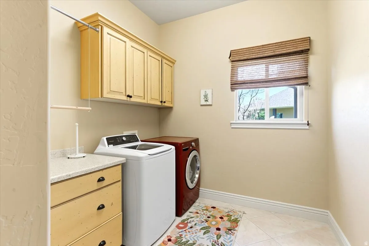 Laundry room featuring upper cabinetry with black hardware, a wood-finish counter with integrated drawers, and a window with a woven Roman shade
