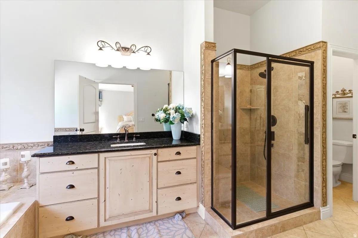 Bathroom featuring a large vanity with a dark countertop and undermount sink, an expansive mirror, and a glass-enclosed shower with tile surround