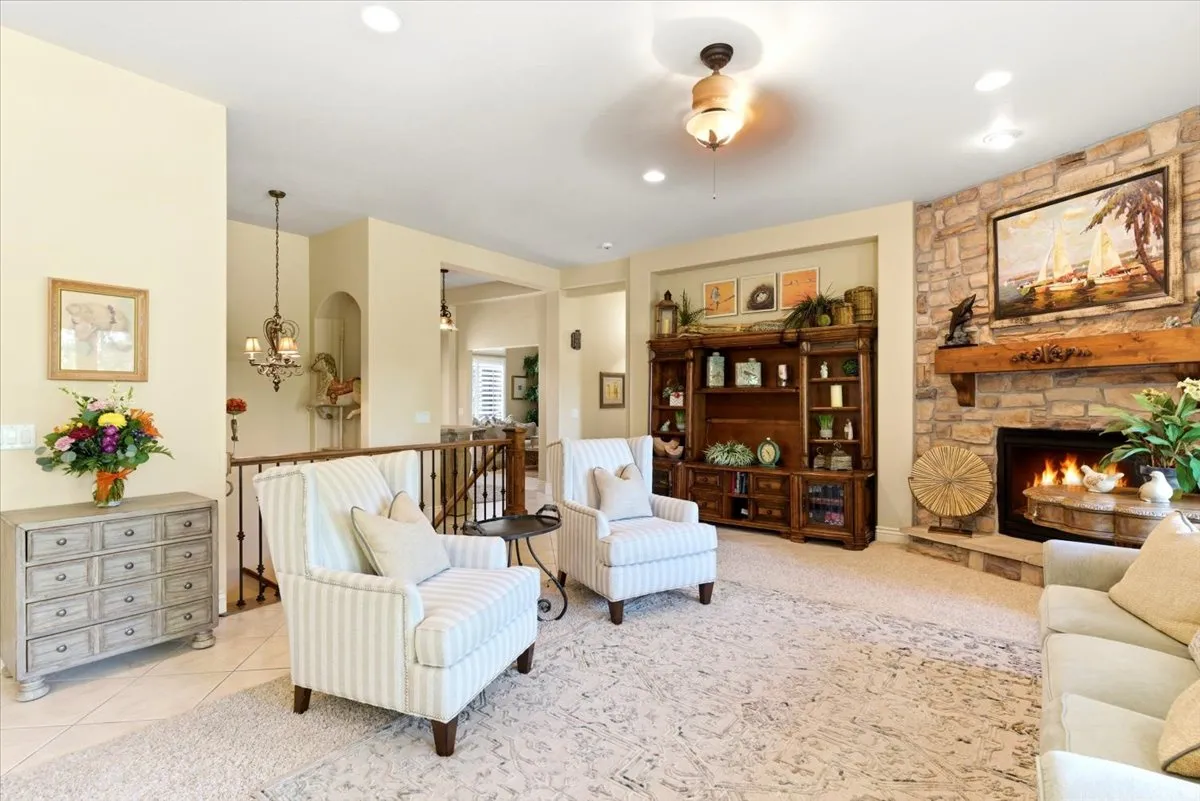 Living area featuring a stone fireplace with a substantial wood mantel, built-in entertainment cabinetry with glass doors, recessed lighting, and a chandelier-style ceiling fixture