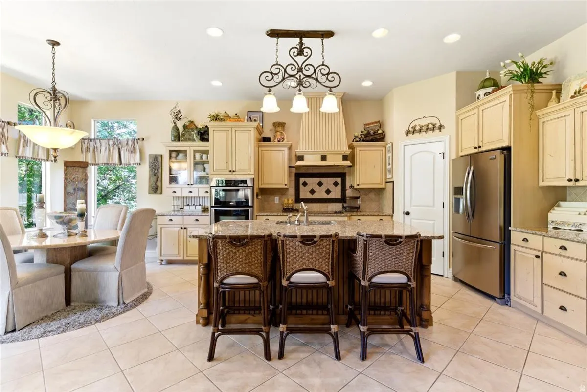 Spacious kitchen featuring a large central island with seating, cream-colored cabinetry, integrated stainless steel appliances, and tile flooring