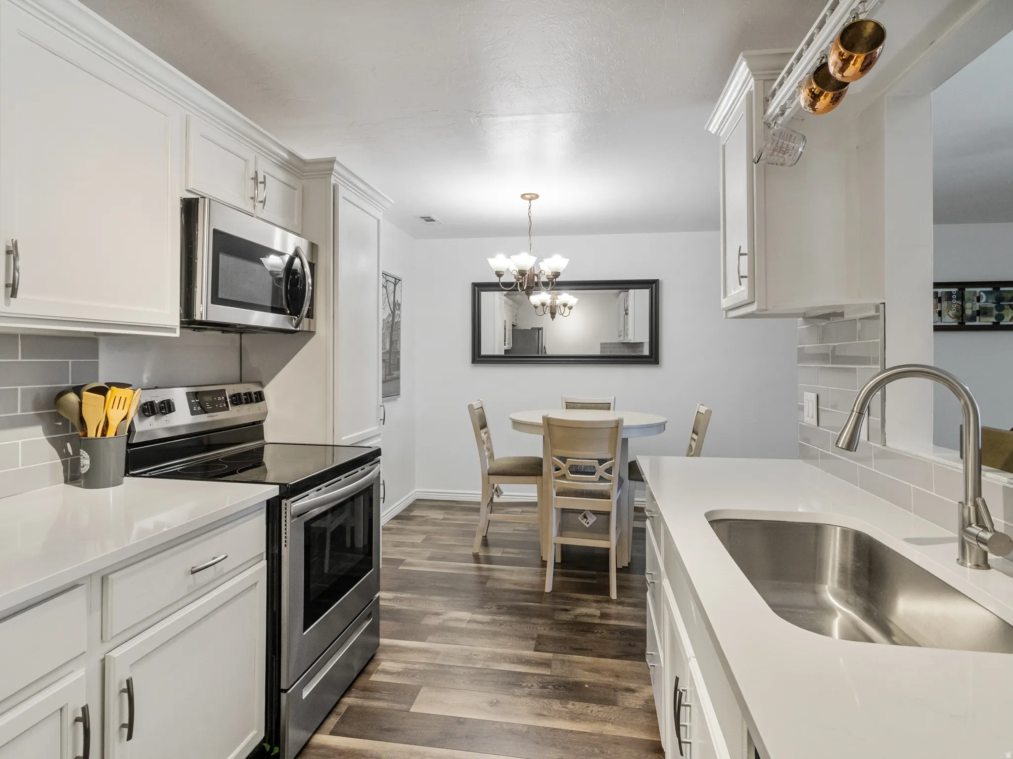 Contemporary kitchen featuring white cabinetry with crown molding, stainless steel appliances, light gray subway tile backsplash, and wood-finish flooring