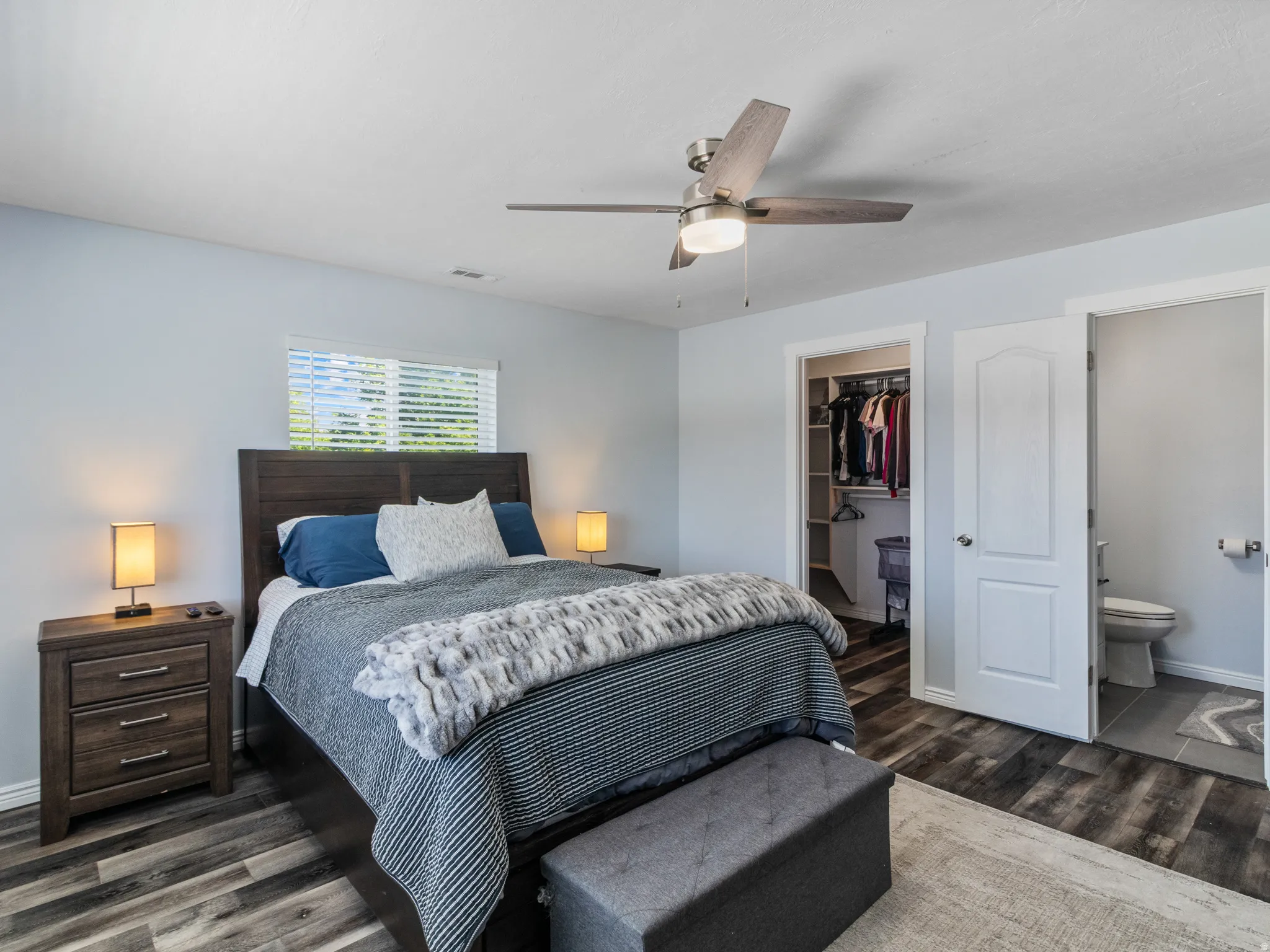 Primary bedroom featuring wood-finish flooring, a ceiling fan, a window with blinds, and a walk-in closet with built-in shelving