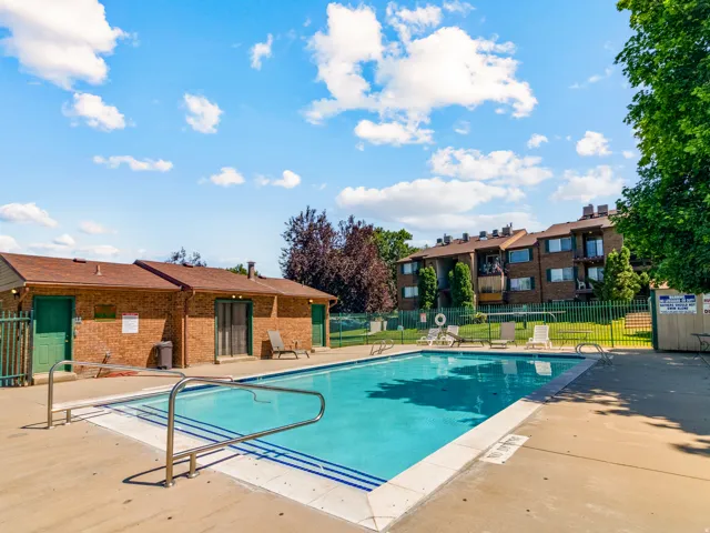 Outdoor swimming pool with concrete surround, metal handrails, and a brick pool house featuring green doors