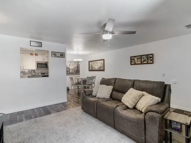 Open-concept living space featuring wood-finish flooring, a ceiling fan with integrated lighting, and a pass-through window to the kitchen