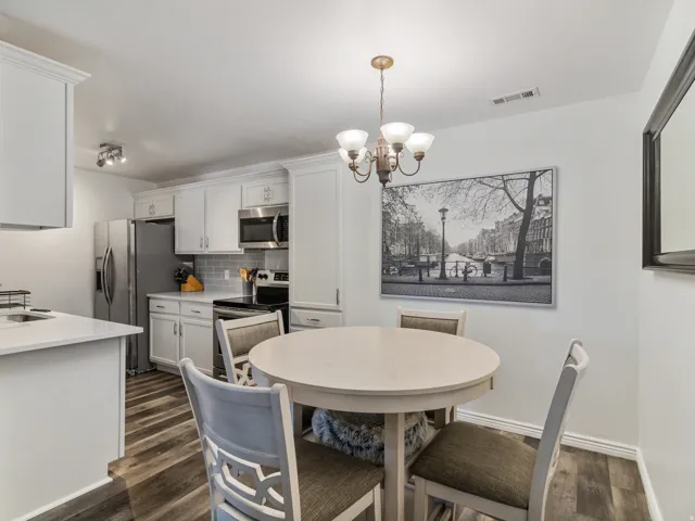 Kitchen and dining area featuring wood-finish flooring, white cabinetry, stainless steel appliances, and a tiled backsplash