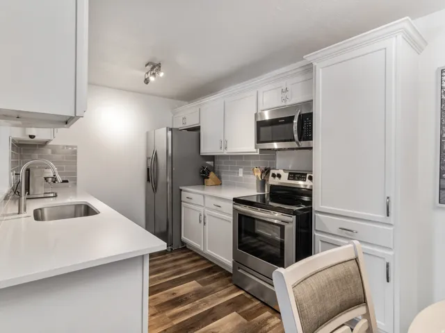 Kitchen featuring white cabinetry with crown molding, stainless steel appliances, light-toned countertops, subway tile backsplash, and wood-finish flooring