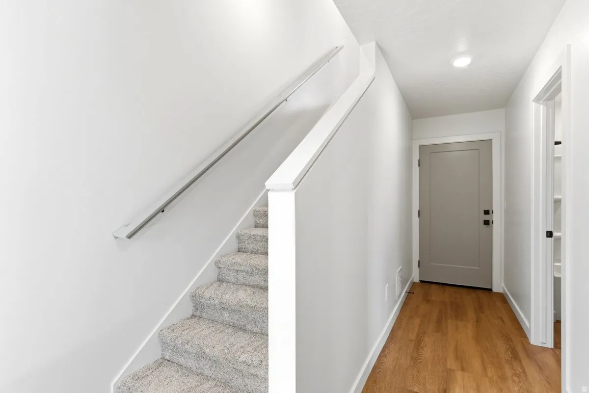 Carpeted staircase with white handrail and a crisp white wall