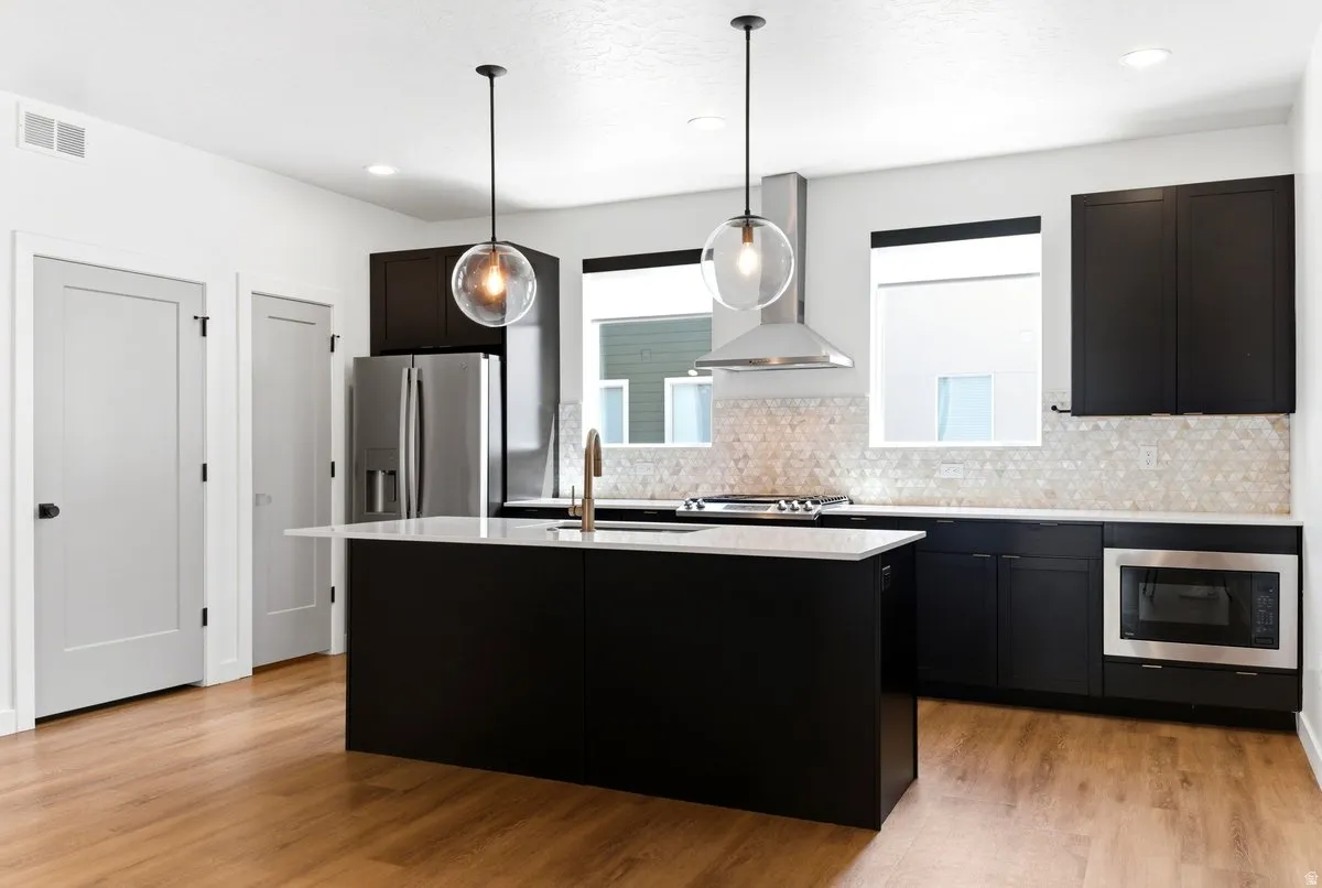 Modern kitchen featuring a central island with a light-colored countertop, dark cabinetry, stainless steel appliances, and wood-finish flooring