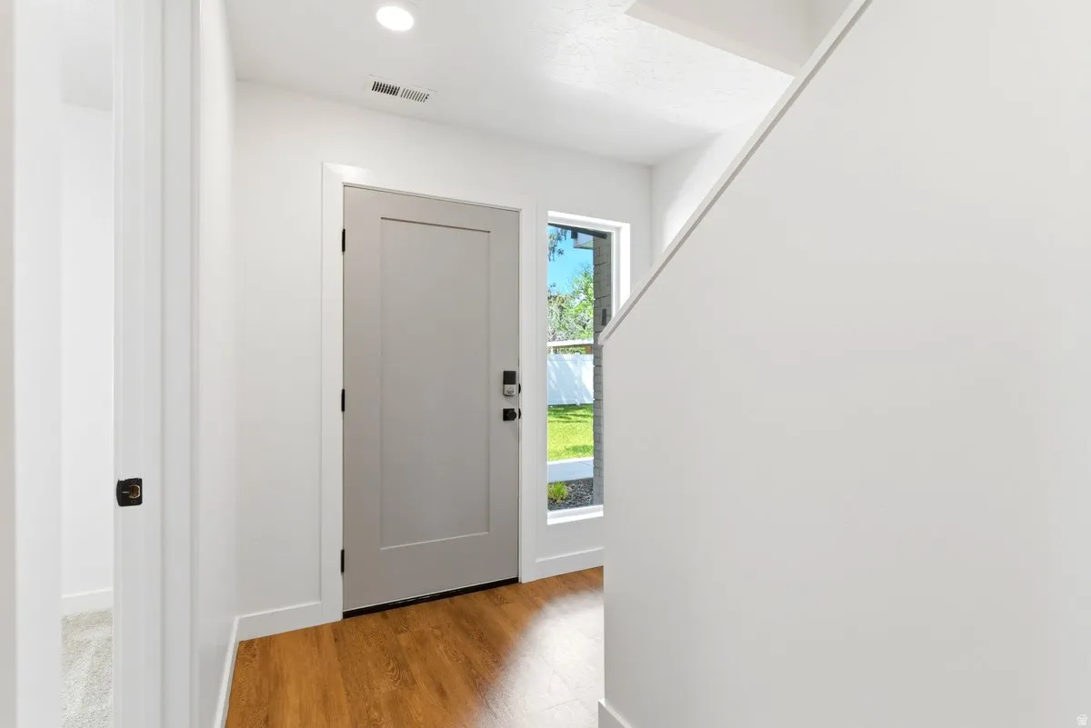 Entryway featuring wood-finish flooring, a contemporary light gray door with black hardware, and an adjacent sidelight window