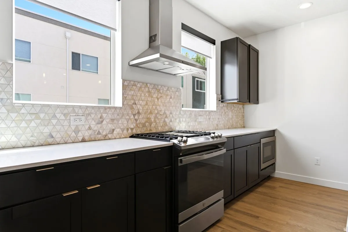 Contemporary kitchen featuring dark cabinetry with gold-toned hardware, light countertops, and a geometric tile backsplash
