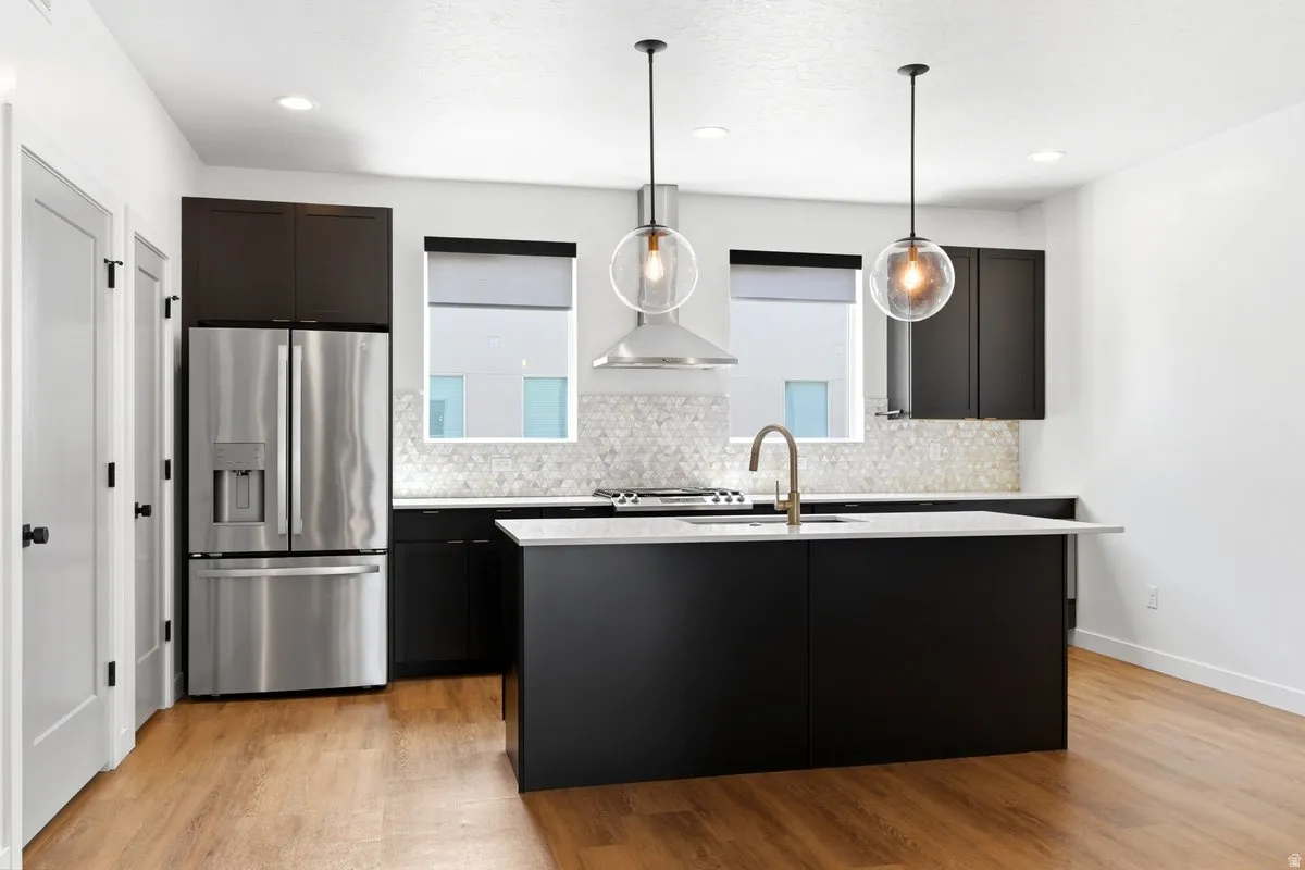 Modern kitchen featuring a central island, stainless steel appliances, black cabinetry, white countertops, and wood-finish flooring