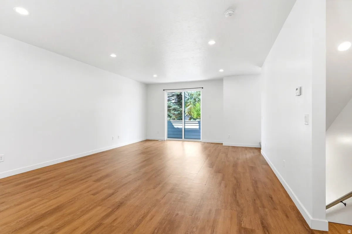 Spacious room featuring wood-finish flooring, recessed lighting, and a sliding glass door providing outdoor access