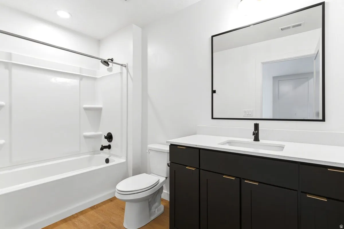 Bathroom featuring a white tub/shower combination with black fixtures, a white toilet, and wood-finish flooring