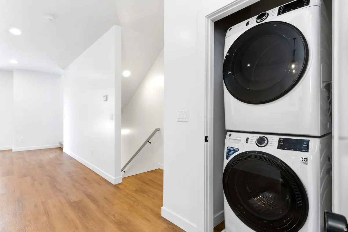 Dedicated laundry closet with stacked washer and dryer, wood-finish flooring, recessed lighting, and a modern stair railing