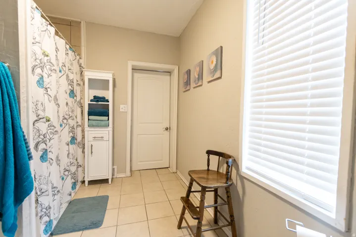 Bathroom featuring a shower with tiled surround, light tan wall paint, tiled flooring, and a window with white blinds