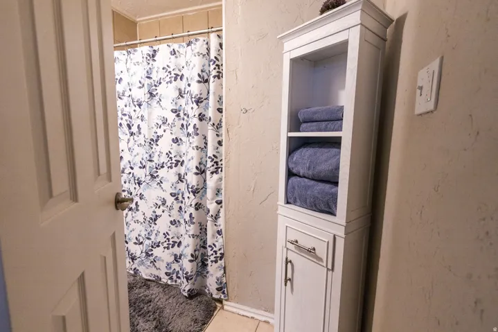 White storage cabinet featuring open shelving and a lower cabinet with brushed nickel hardware