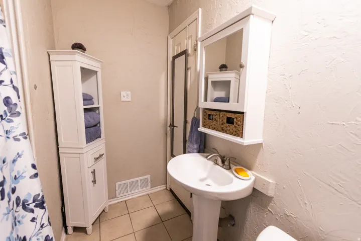 Pedestal sink with chrome hardware, complemented by a mirrored medicine cabinet featuring integrated shelving