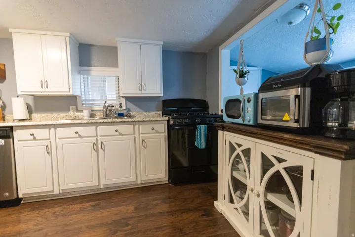 Kitchen with wood-finish flooring, white cabinetry, a built-in dishwasher, and a black range