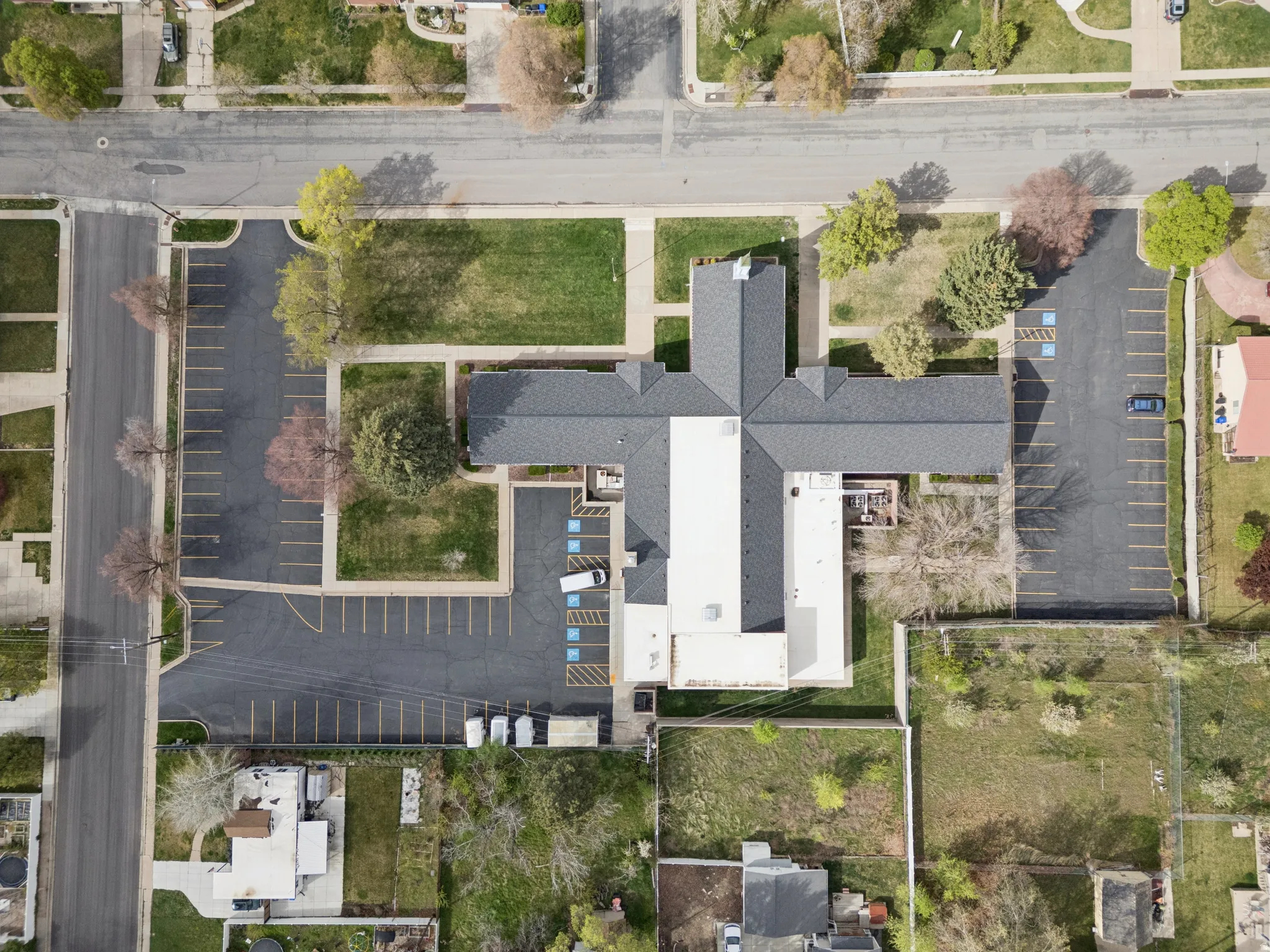 Aerial view of property with structure, paved parking lot with clearly marked stalls, and trees.