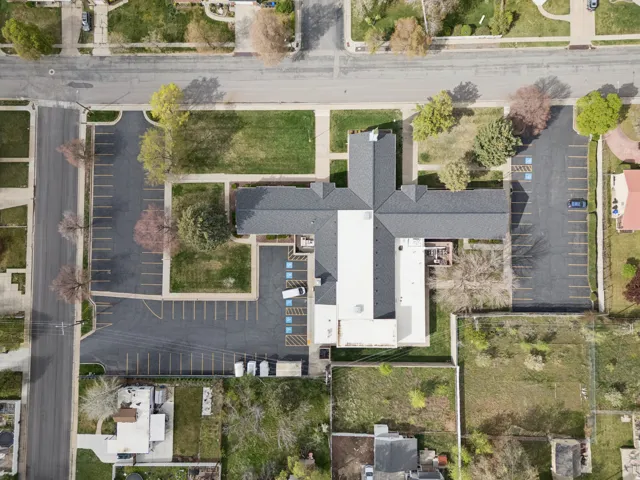 Aerial view of property with structure, paved parking lot with clearly marked stalls, and trees.