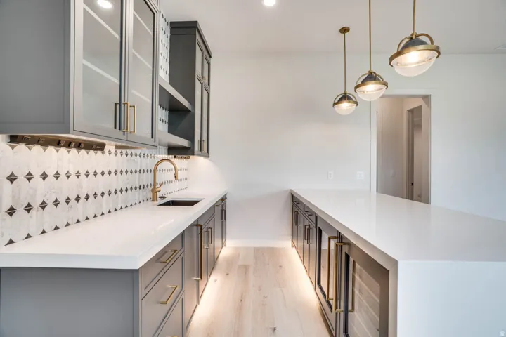 Contemporary wet bar featuring light wood-finish flooring, a white countertop, and dark gray cabinetry with brass hardware