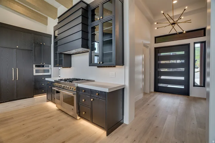 Modern kitchen and entryway featuring a professional-grade range, custom dark wood cabinetry with gold-tone hardware, and light wood-finish flooring